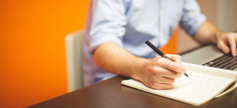 man writing information from a computer onto paper